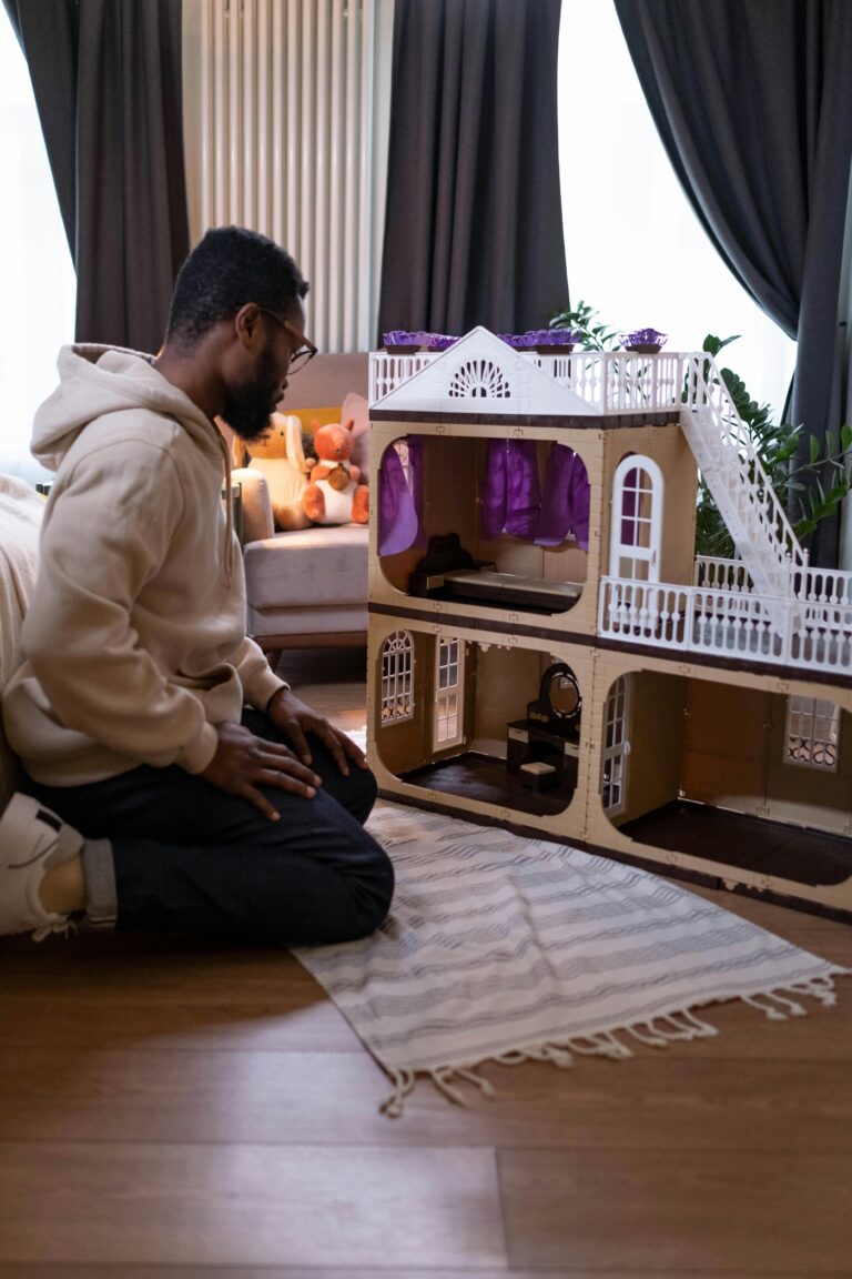 A father kneeling and attentively playing with a dollhouse in a cozy room.